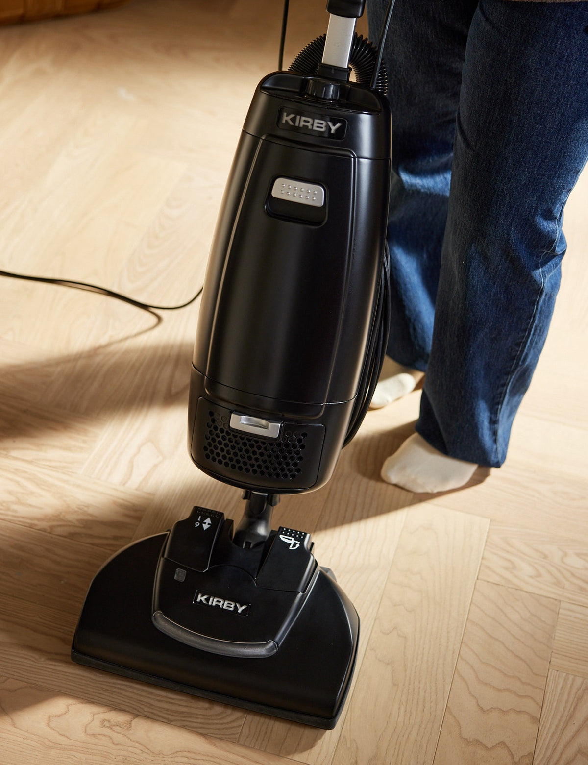 A black Kirby Signature Series V530 upright vacuum cleaner being used on a light wood floor.