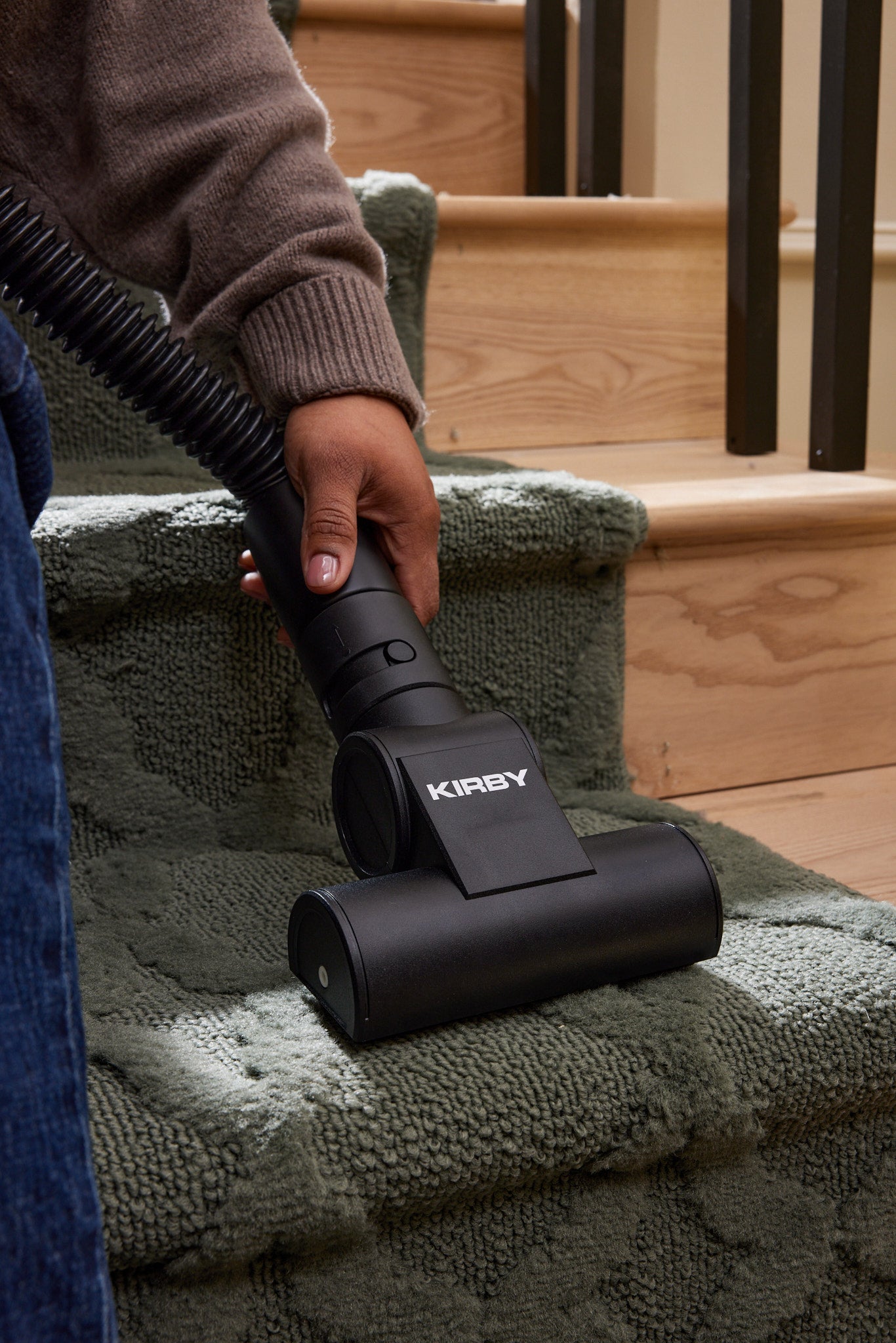 A woman using a Kirby Signature Series C530 canister vacuum to clean carpeted indoor stairs with a black vacuum nozzle attachment.