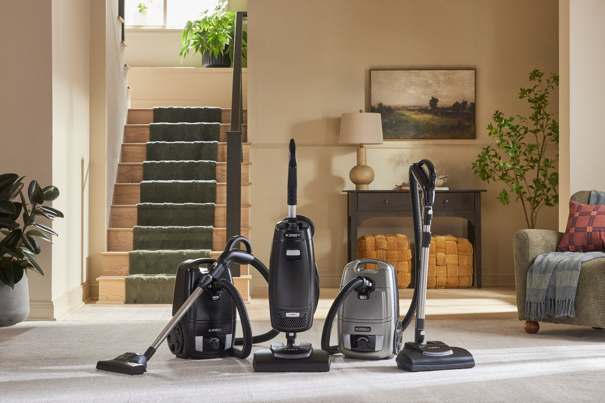 Kirby Signature Series vacuum cleaners lined up in the living room atop a carpeted floor.