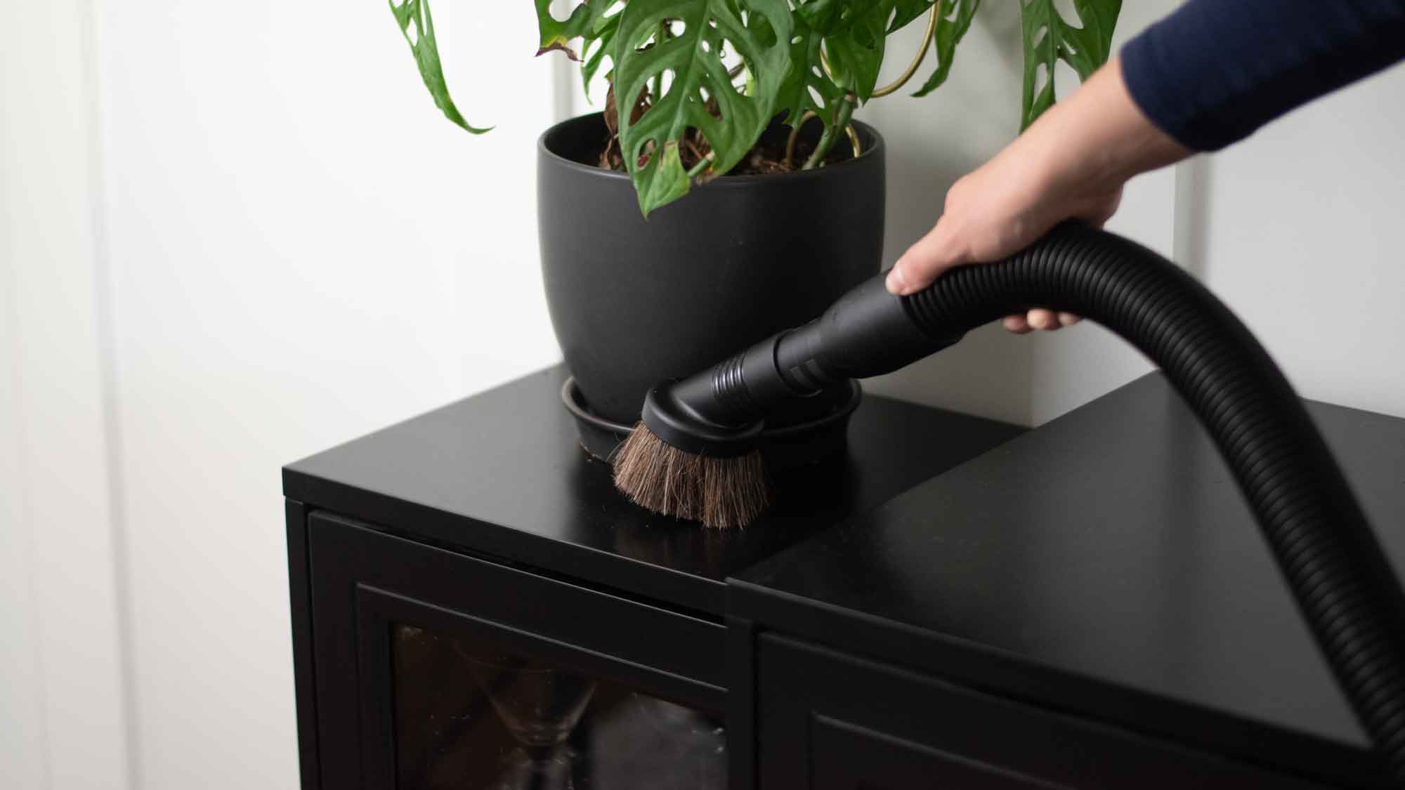 A person using Kirby's duster brush attachment to clean a shelf
