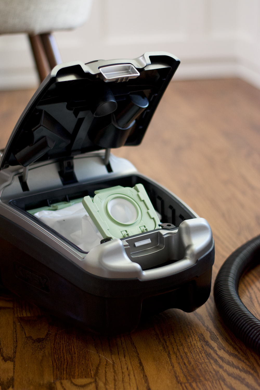 A close-up of a Kirby Signature Series C530 canister vacuum cleaner's PureAir Dual-HEPA filter bag, placed on a wooden floor with a vacuum hose visible on the right.