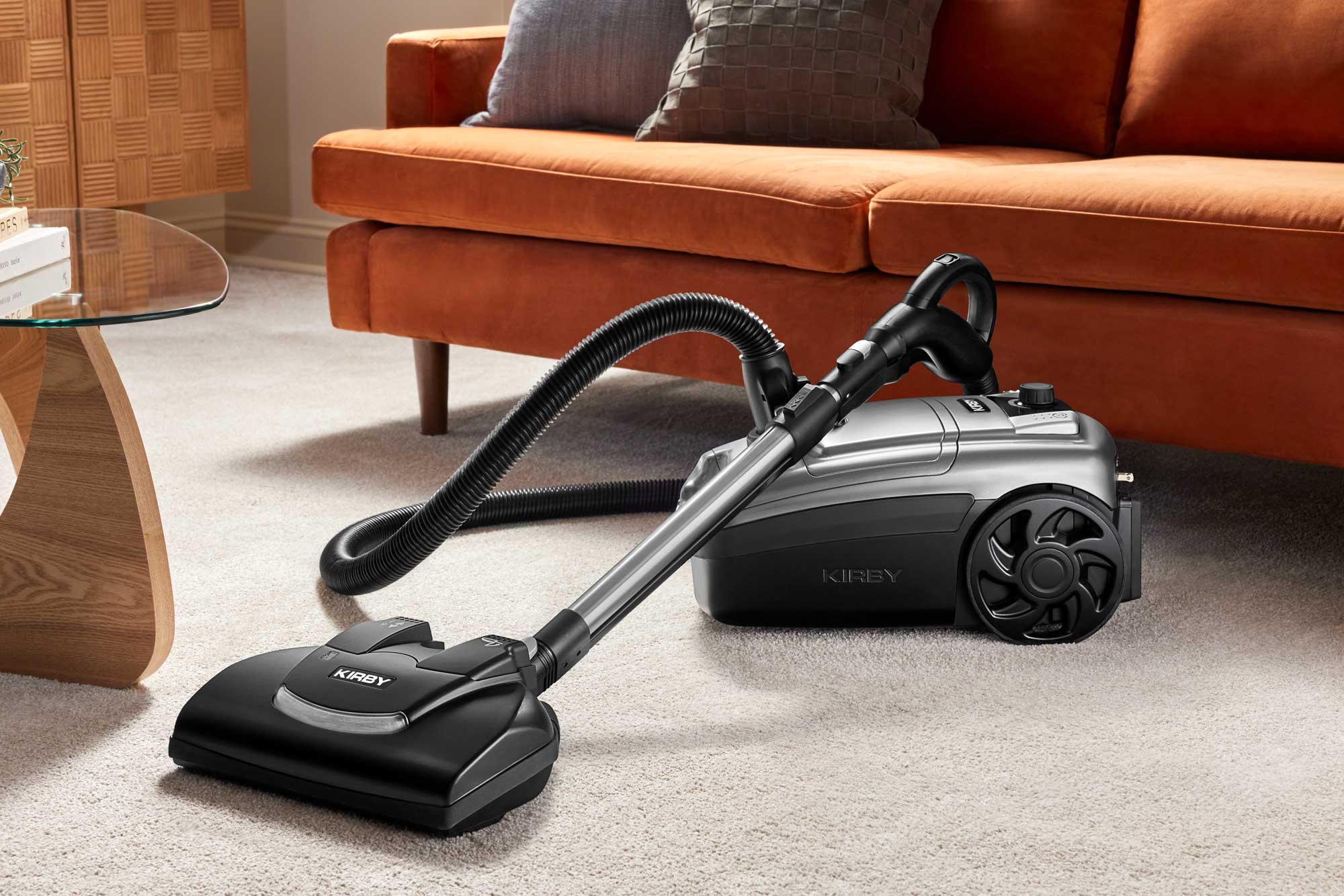 Kirby Signature Series C550 canister vacuum in black and platinum, with multi-surface Power Nozzle attached, positioned on a light beige carpet in a living room setting.