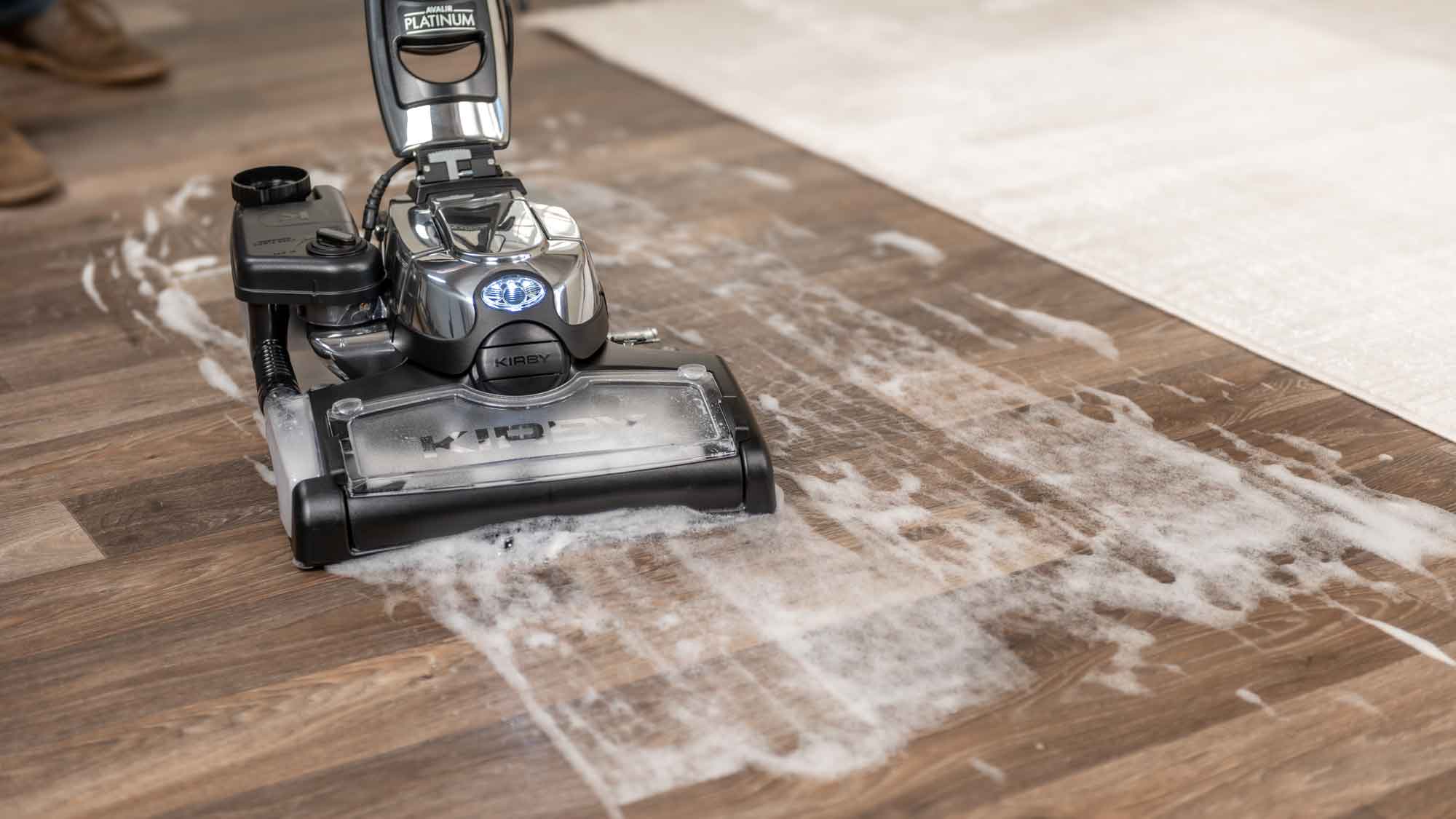 Kirby Avalir Platinum upright vacuum in silver and black, cleaning a hardwood floor.