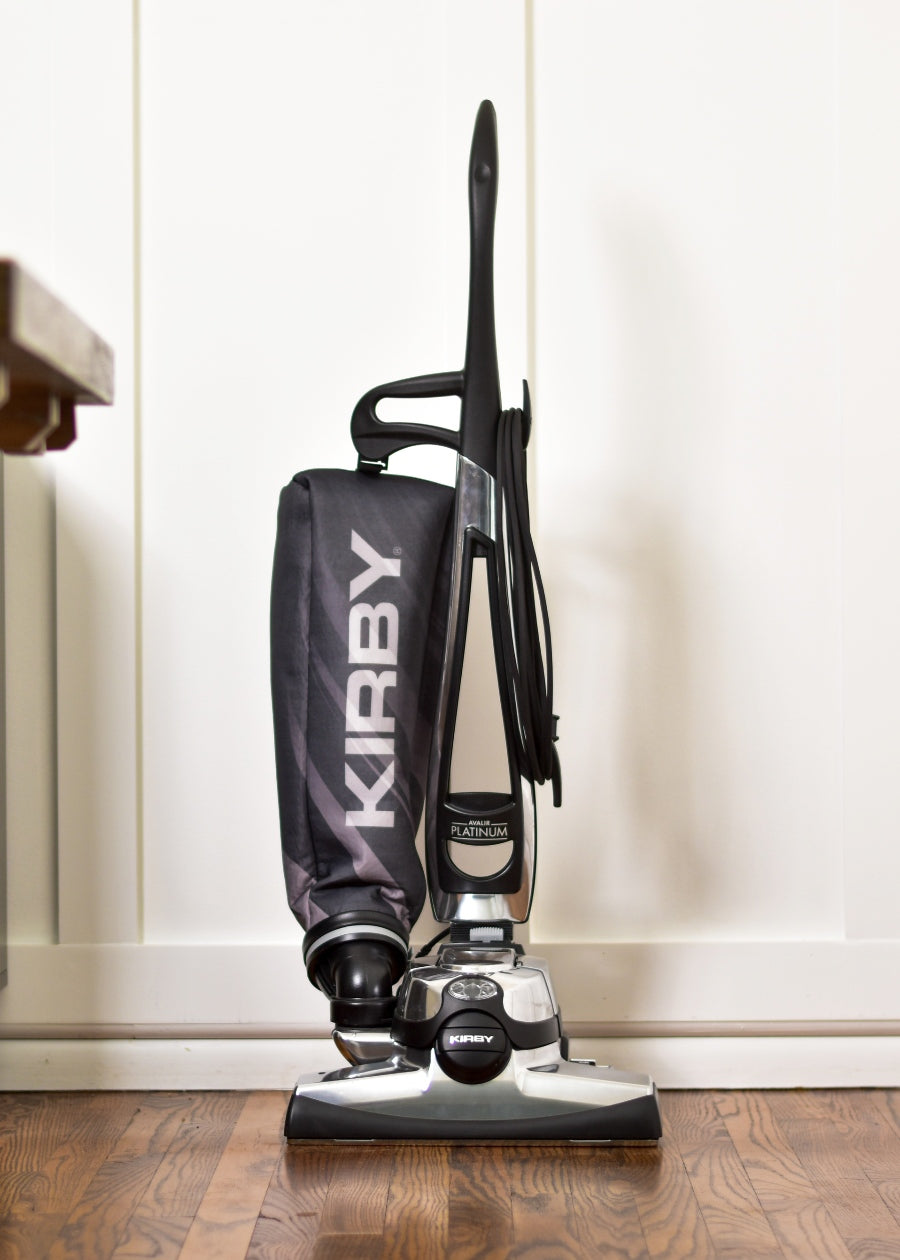 Kirby Avalir Platinum upright vacuum, black and silver, standing on a wooden floor.