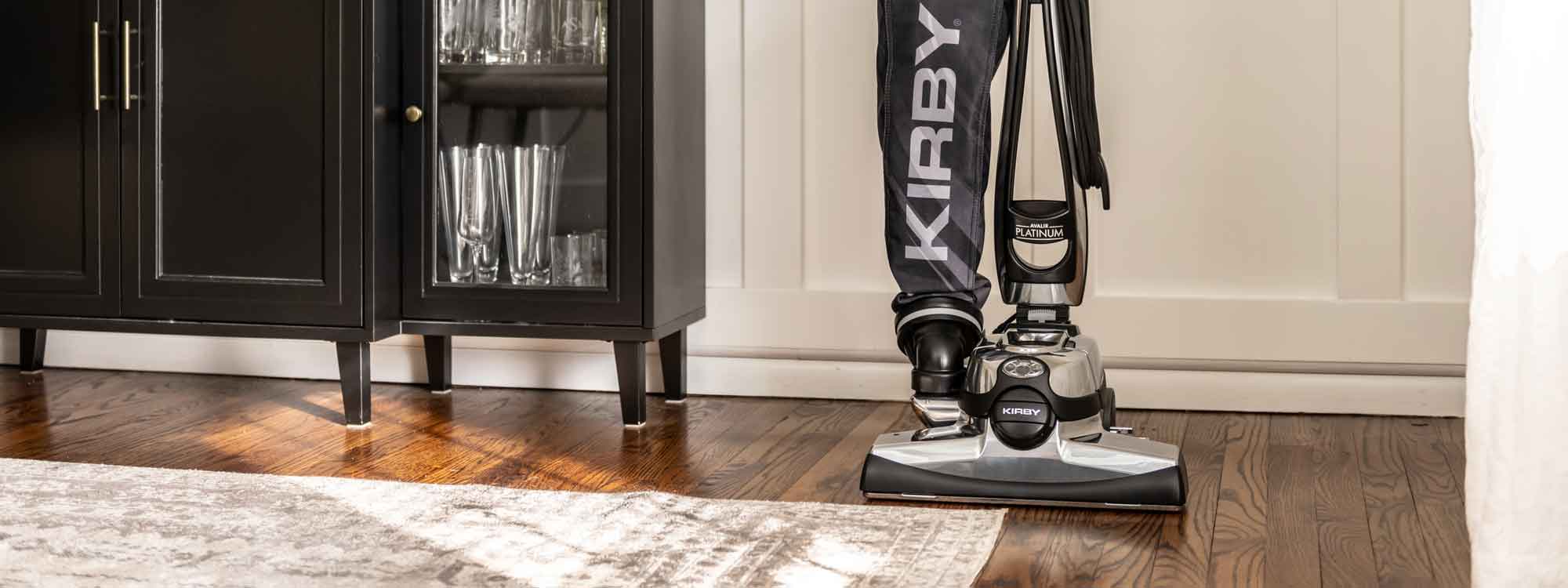 A Kirby vacuum that is sitting on the floor in front of a cabinet