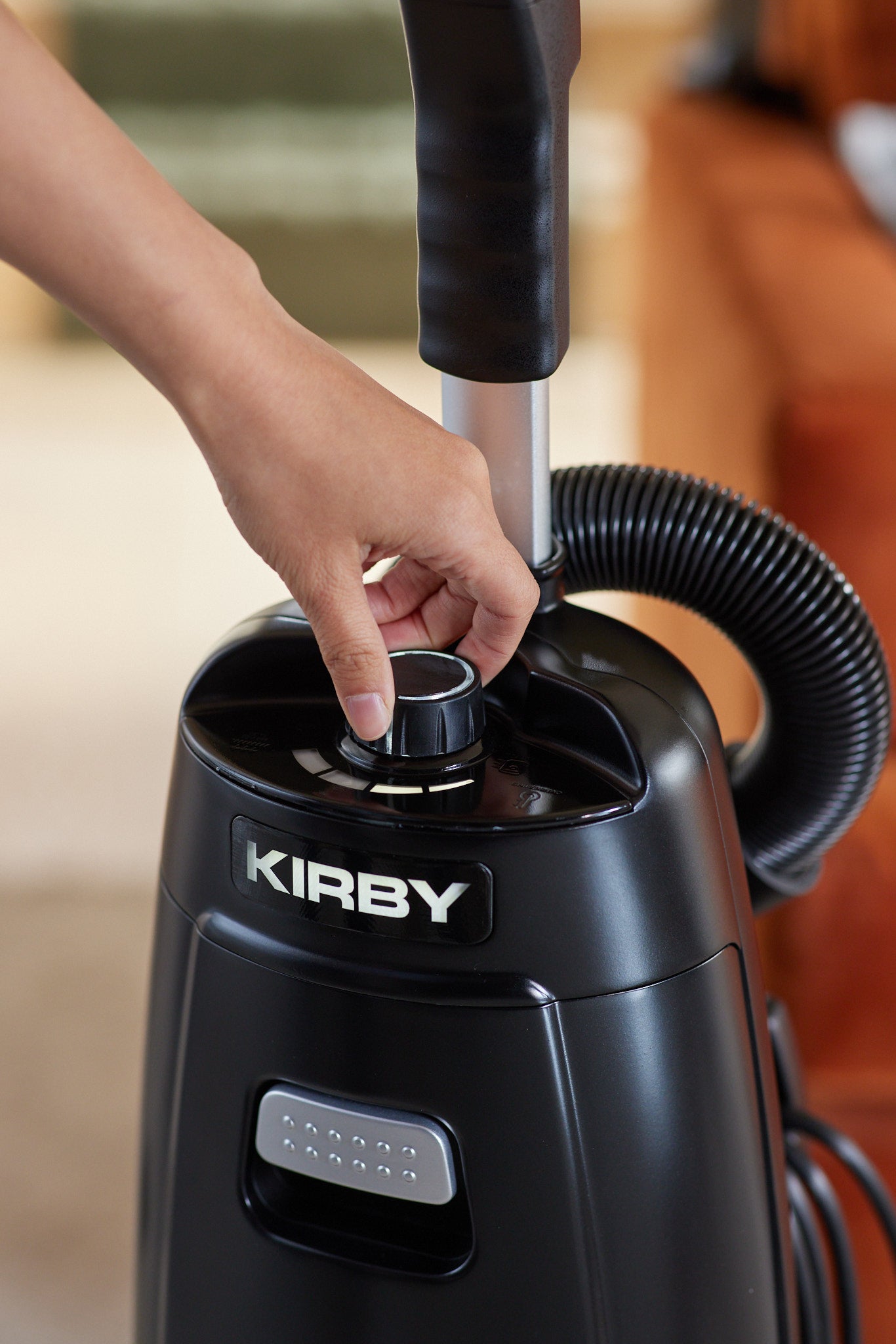 A close-up of a woman's hand adjusting the 4-Speed Airflow Control knob on a black Kirby Signature Series V530 upright vacuum.