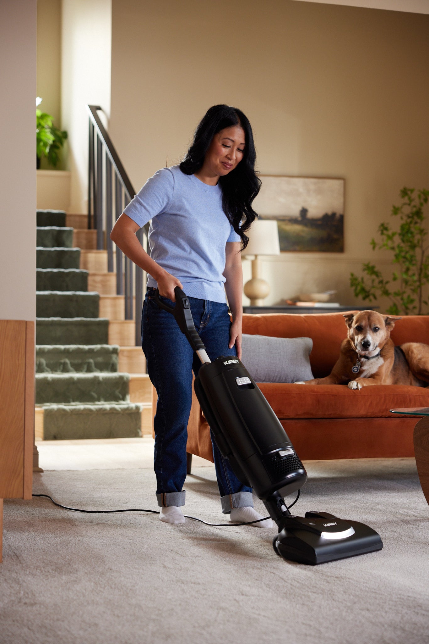 A woman using a Kirby Signature Series V530 upright vacuum to clean a beige carpet in a living room.