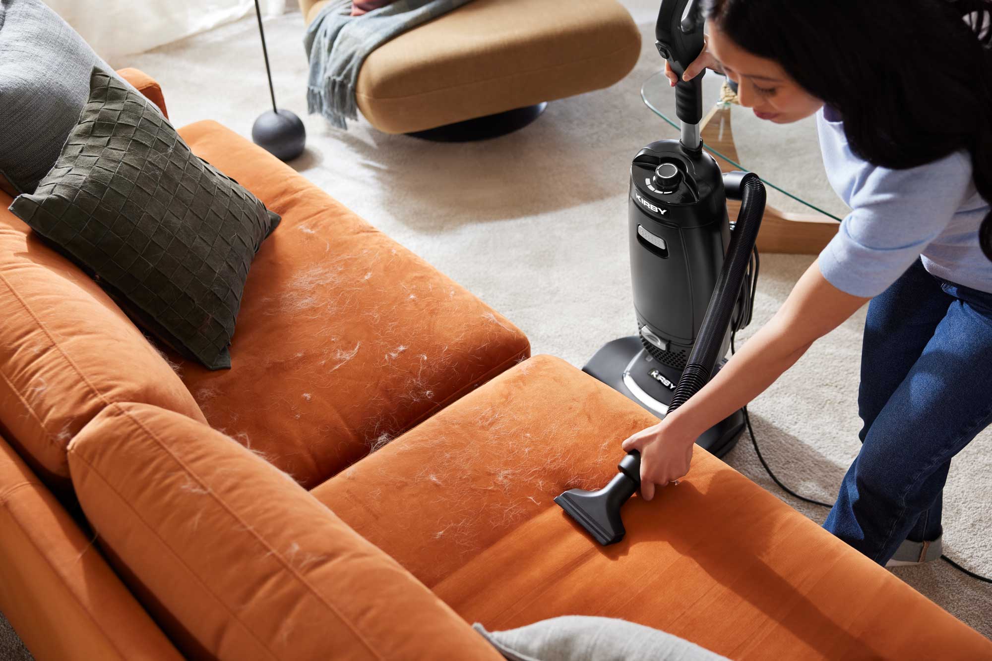 Woman vacuuming orange couch covered in pet hair with the Kirby V530 Upright Vacuum