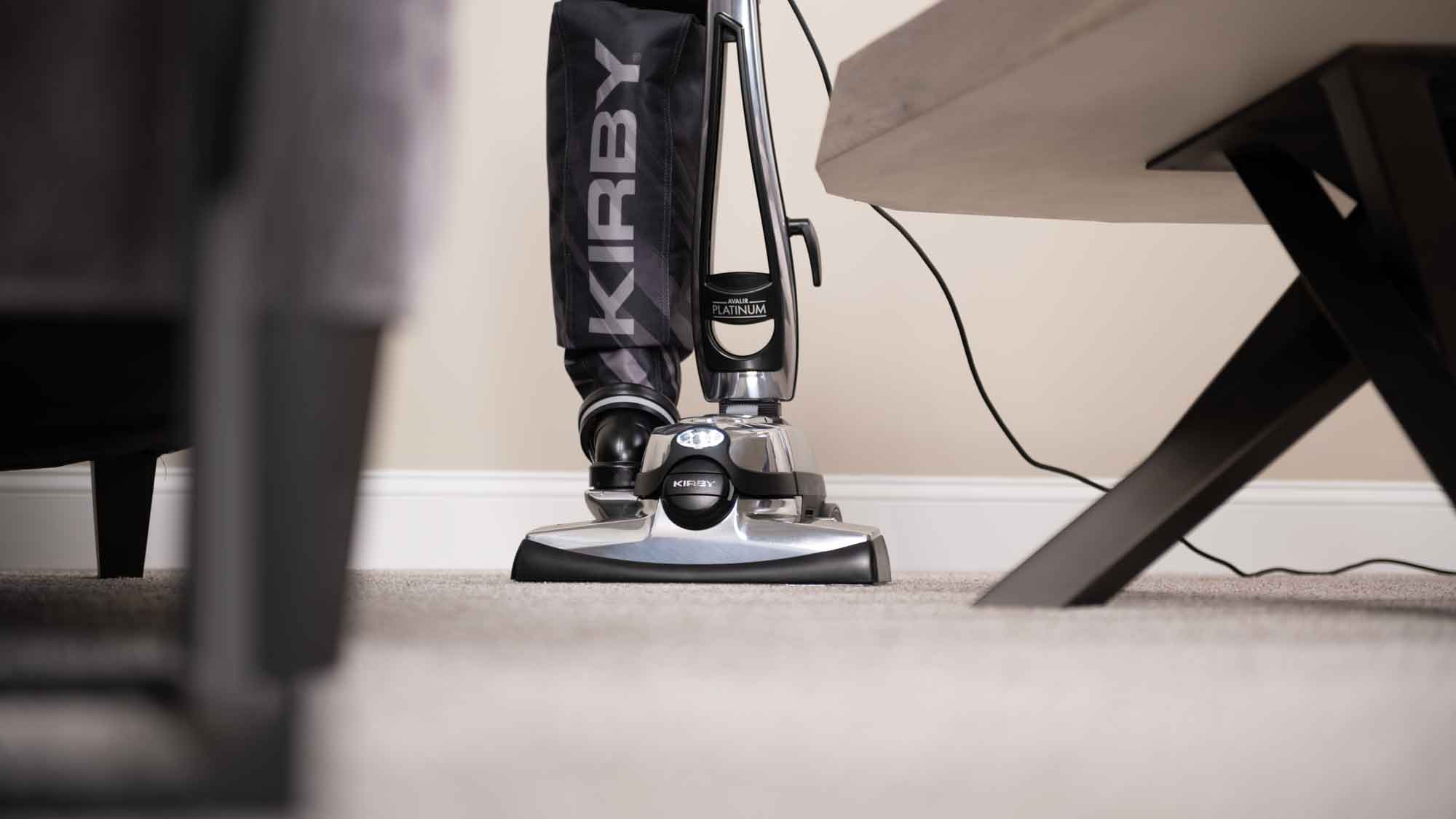 A Kirby vacuum that is sitting on the floor next to a chair