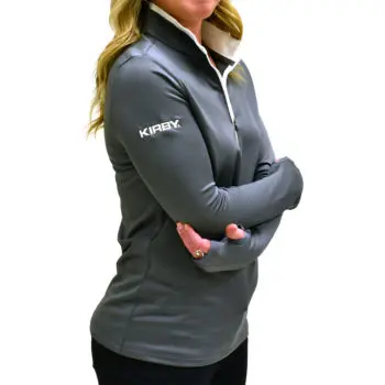 Woman wearing a gray Kirby pullover with white zipper and logo on the sleeve.