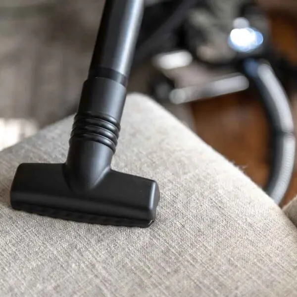 Black Kirby vacuum attachment cleaning a light gray upholstered chair.