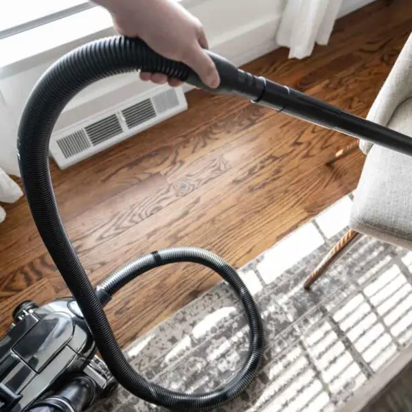 Person using a black Kirby vacuum on a beige upholstered chair.