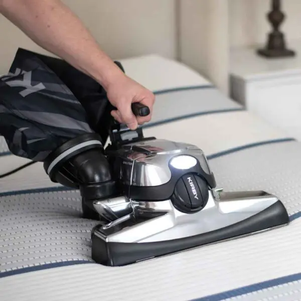 Person using a Kirby Avalir Platinum vacuum on a mattress.