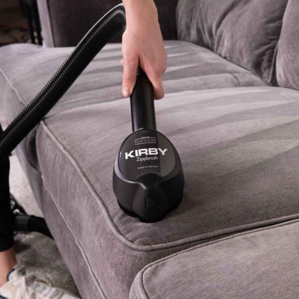 Person using a black Kirby Zippbrush on a gray couch.