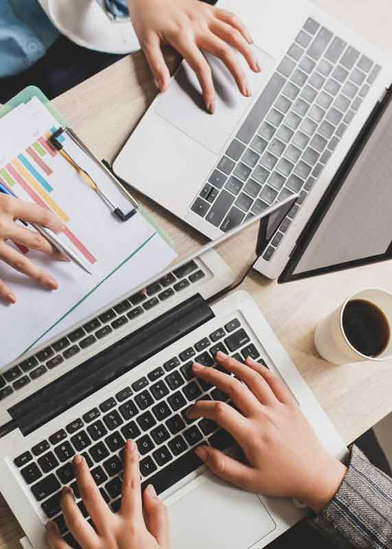 Two people working on laptops with documents and a cup of coffee on a wooden table.