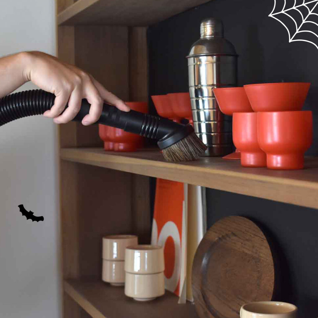 A person using Kirby's duster brush attachment to clean a shelf