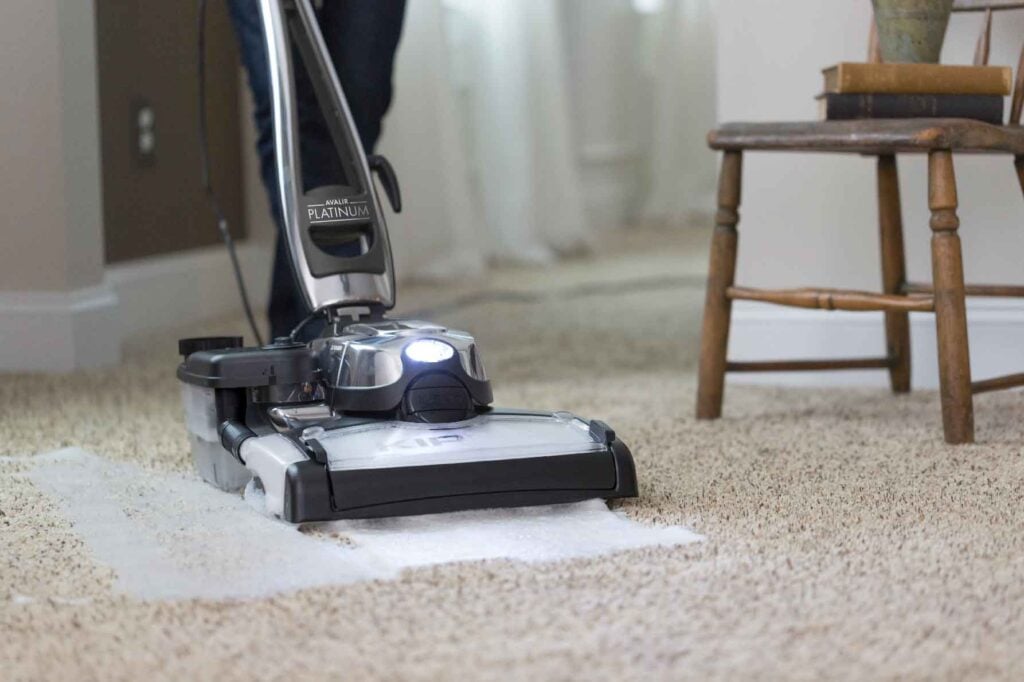 Kirby vacuum cleaner in silver and black, cleaning a beige carpet.