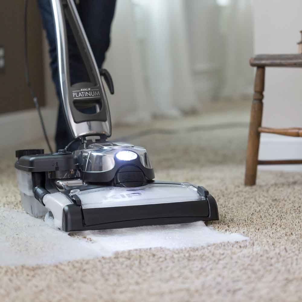 Kirby vacuum in silver and black, cleaning a beige carpet.