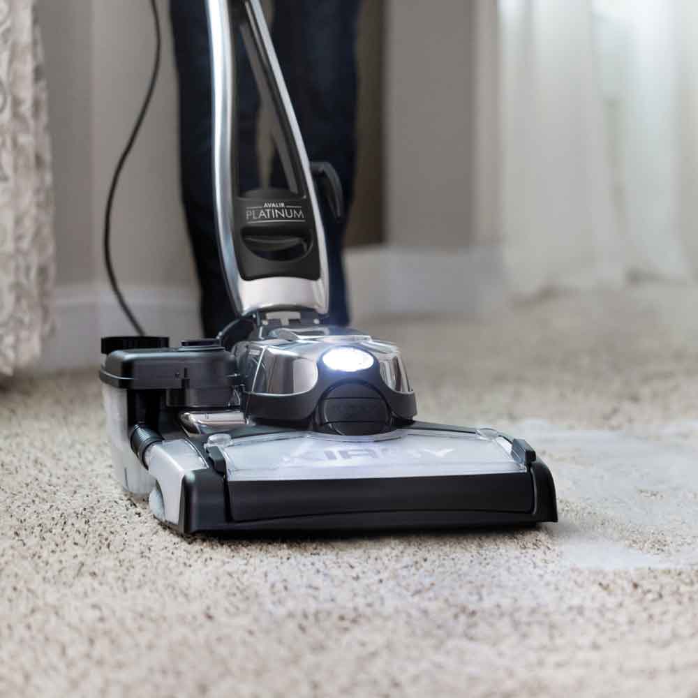 Kirby vacuum cleaner in silver and black, cleaning a beige carpet.