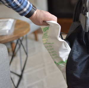 Hand installing a white and green Kirby HEPA bag into a black vacuum cleaner.