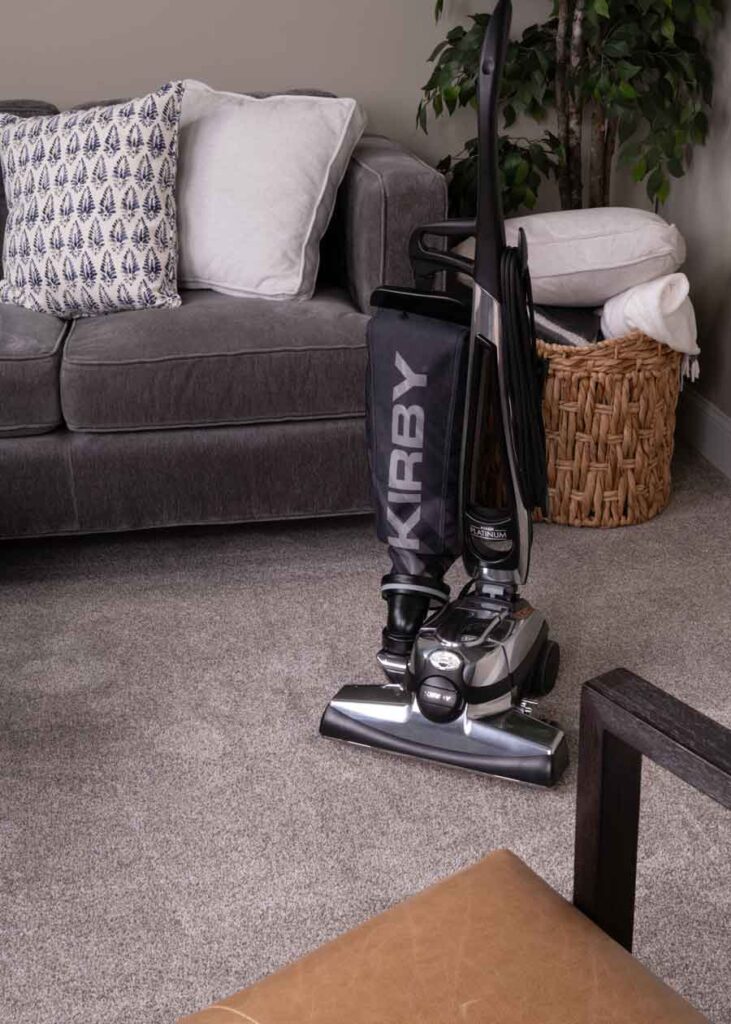 Kirby Avalir Platinum vacuum cleaner on carpet near a gray couch with pillows.