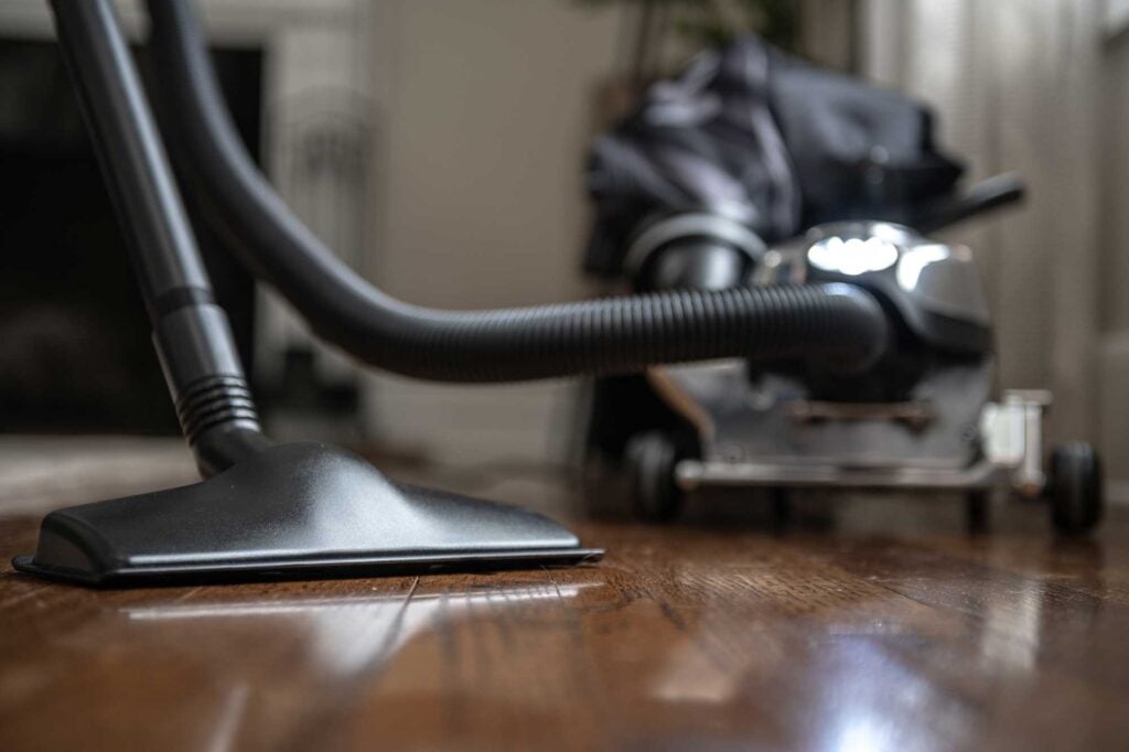 Kirby vacuum cleaner with a black floor nozzle and a silver body on a wooden floor.