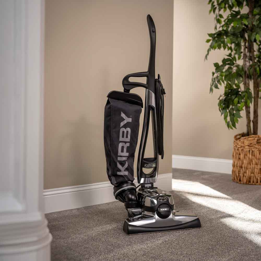 Kirby Avalir Platinum upright vacuum, black and silver, standing on a carpeted floor.