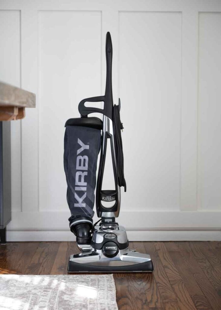 Kirby Avalir Platinum upright vacuum, black and silver, standing on a wooden floor.