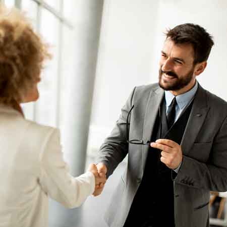 Two business people shaking hands, one holding glasses.