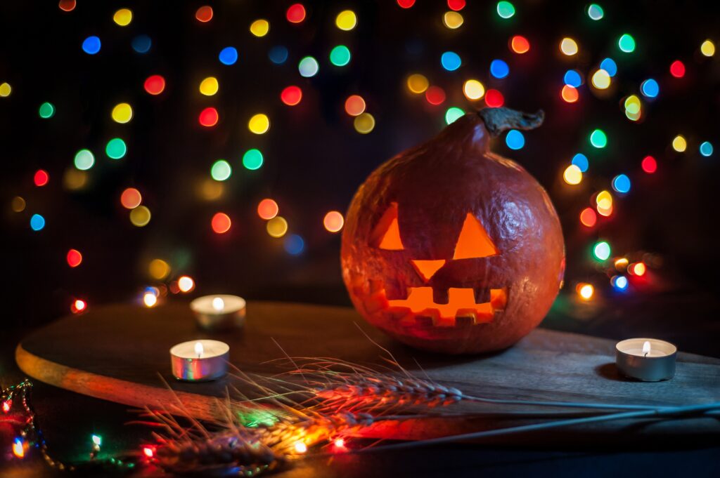 A jack o'lantern sitting on a table with candles and colorful lights in the backgroud