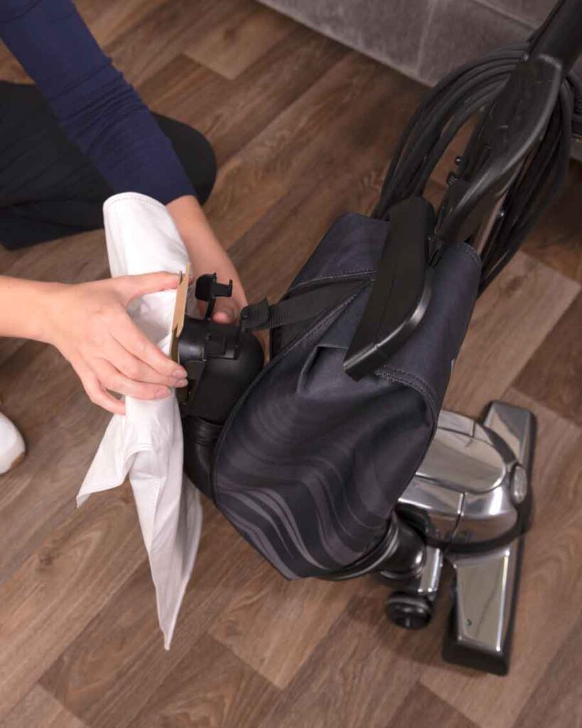 Person installing a white HEPA filter into a black Kirby vacuum cleaner.