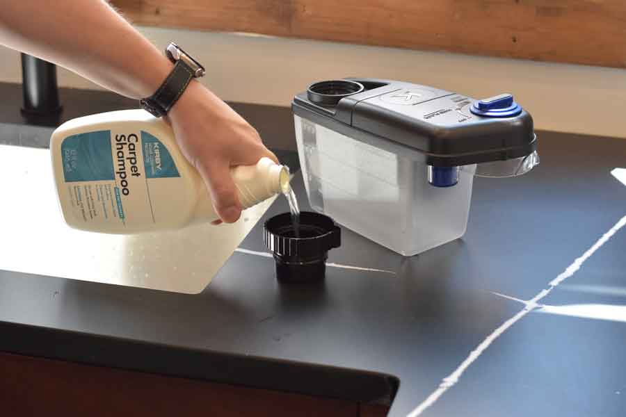 Person pouring Kirby Carpet Shampoo into the Kirby Multi-Surface Shampoo System vacuum accessory.