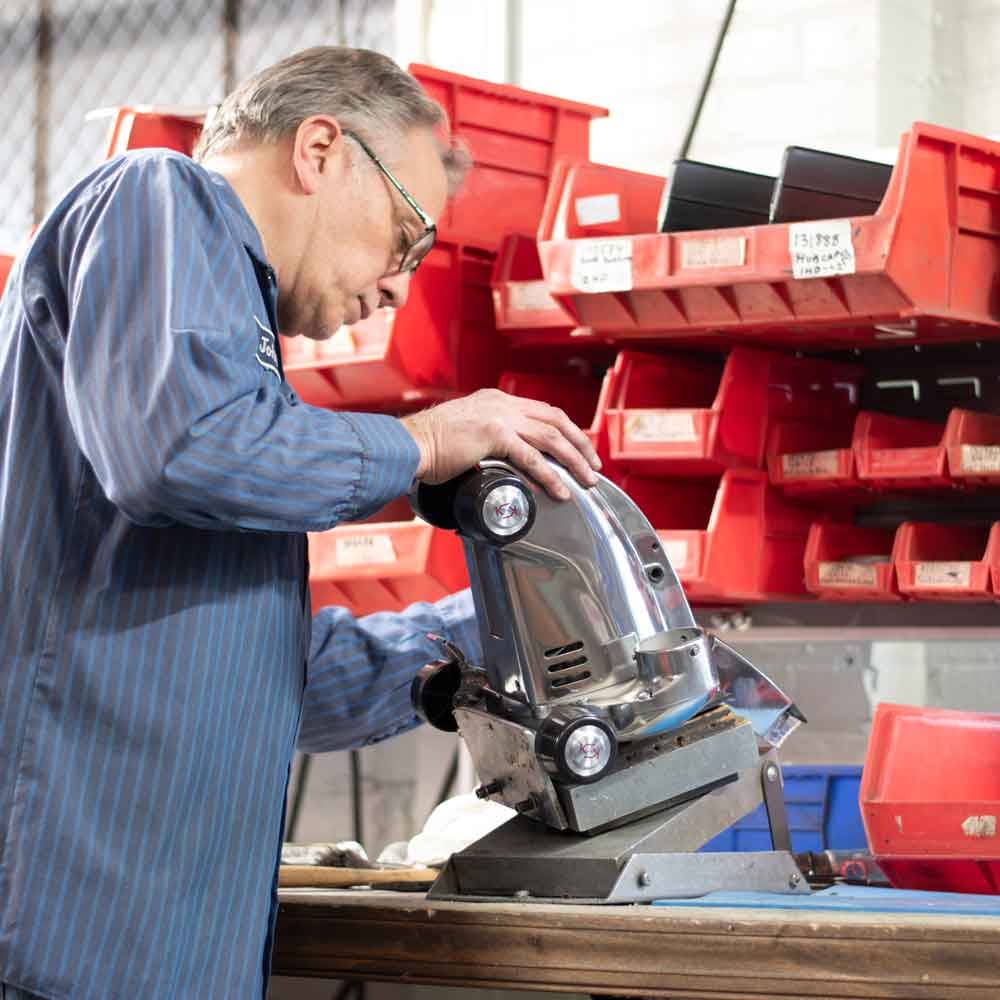 Man working on a silver Kirby vacuum cleaner in a workshop.