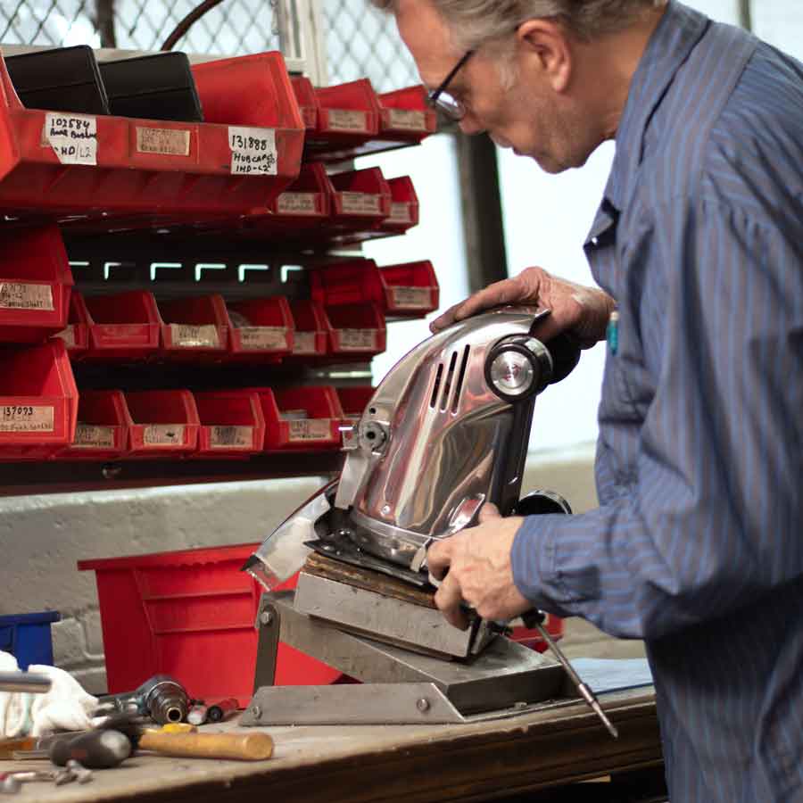 Man working on a silver Kirby vacuum cleaner in a workshop.