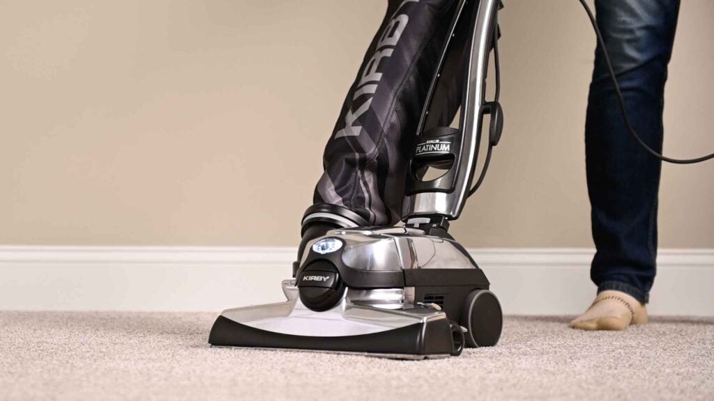 Kirby vacuum cleaner in black and silver, cleaning a beige carpet.