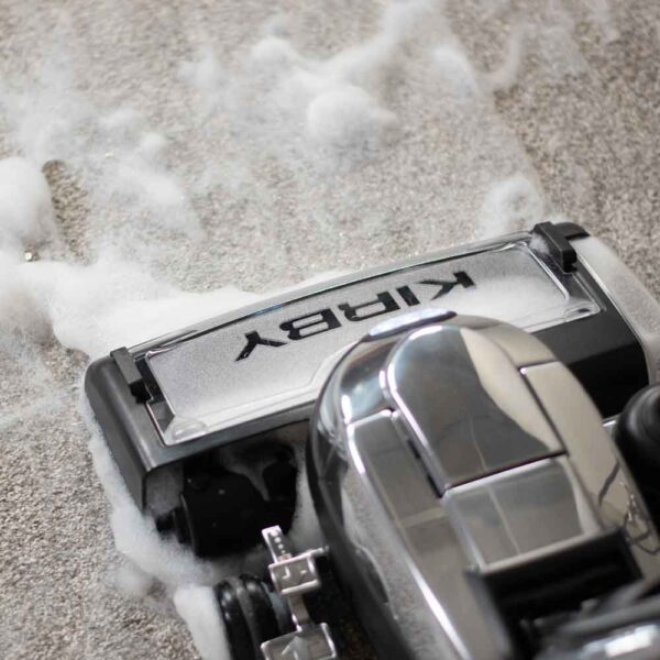 Kirby vacuum shampooing carpet, silver and black.