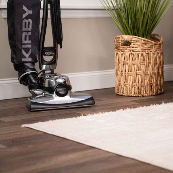 Kirby Avalir Platinum upright vacuum on wooden floor next to a white rug and wicker basket.