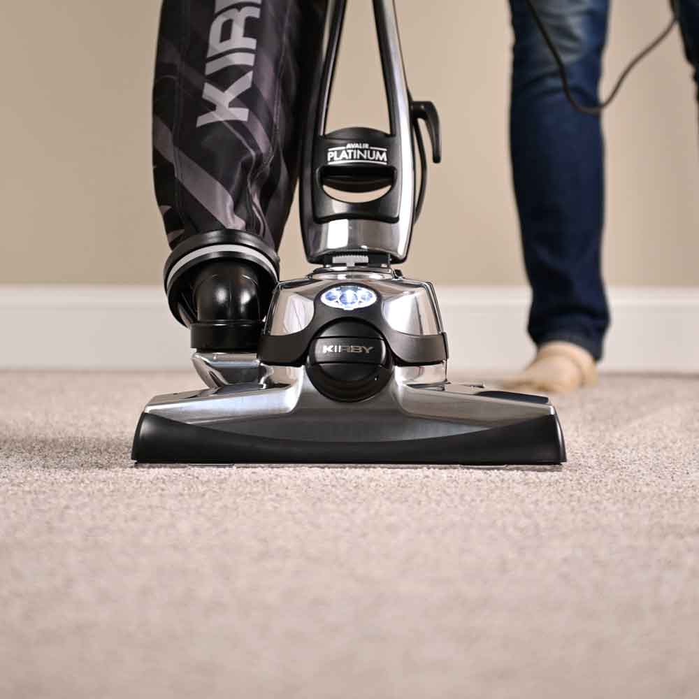 Kirby vacuum cleaner in silver and black, cleaning a carpet.