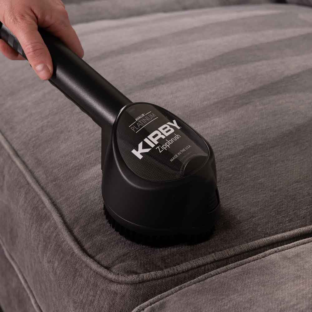 A person using Kirby's ZippBrush to clean a couch