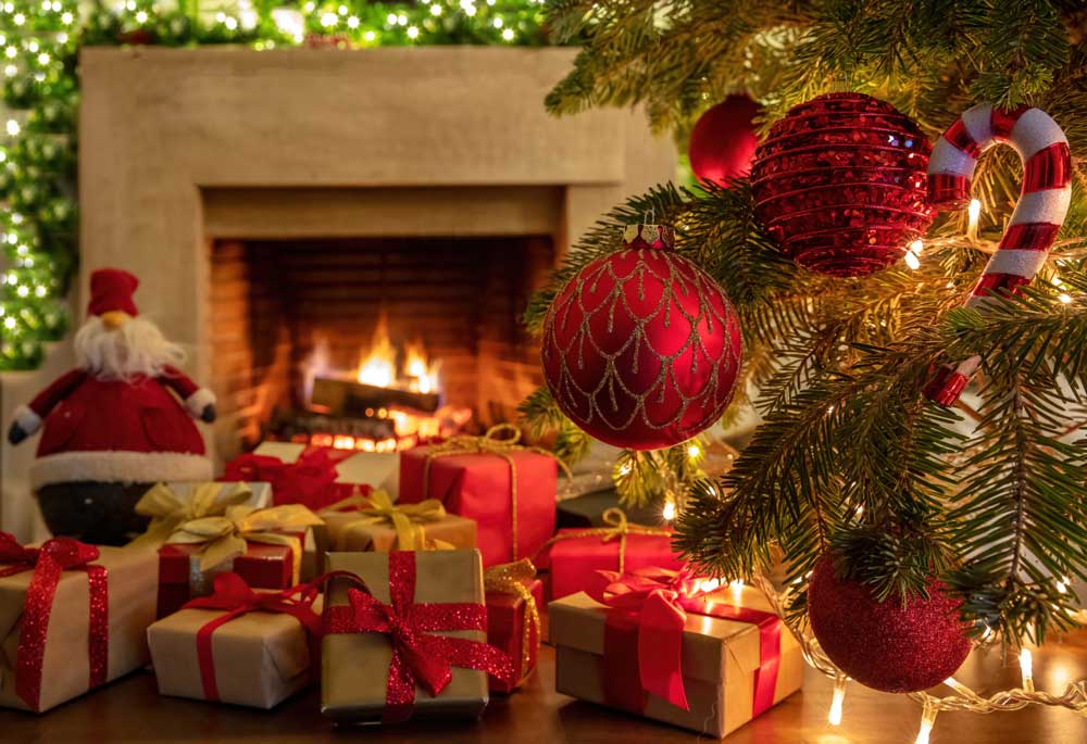 Xmas celebration and presents concept. Christmas lights, tree branch with red balls, Santa Claus doll, gift boxes with sparkle ribbons and blur burning fireplace background. Warm family moments.